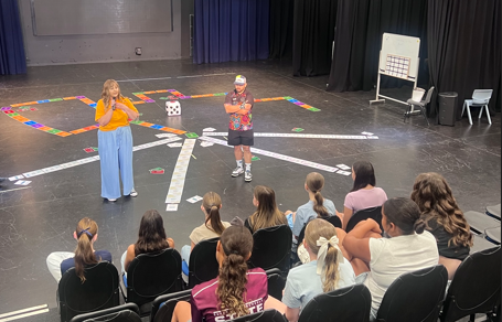Kayla facilitating a life sized board game workshop with a group of students seated around the floor